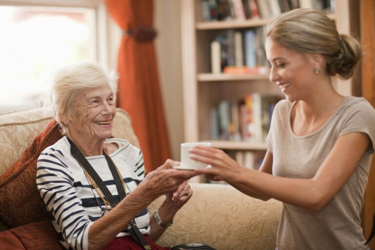 Care assistant handing coffee cup to senior woman