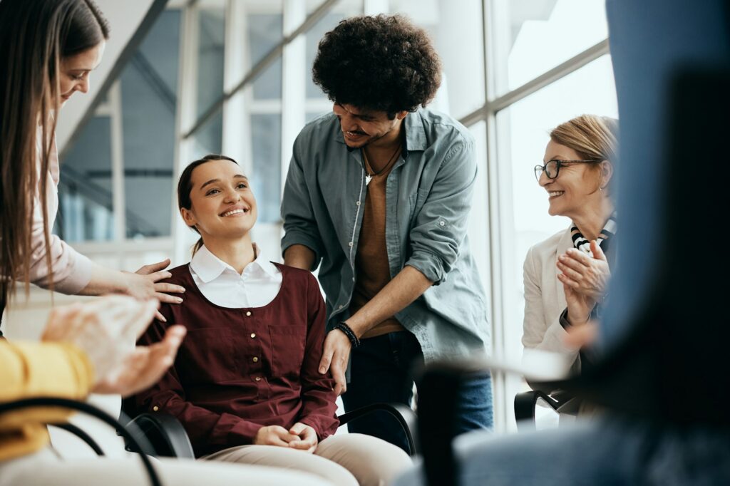 Supportive people encouraging young woman during group therapy meeting at mental health center.